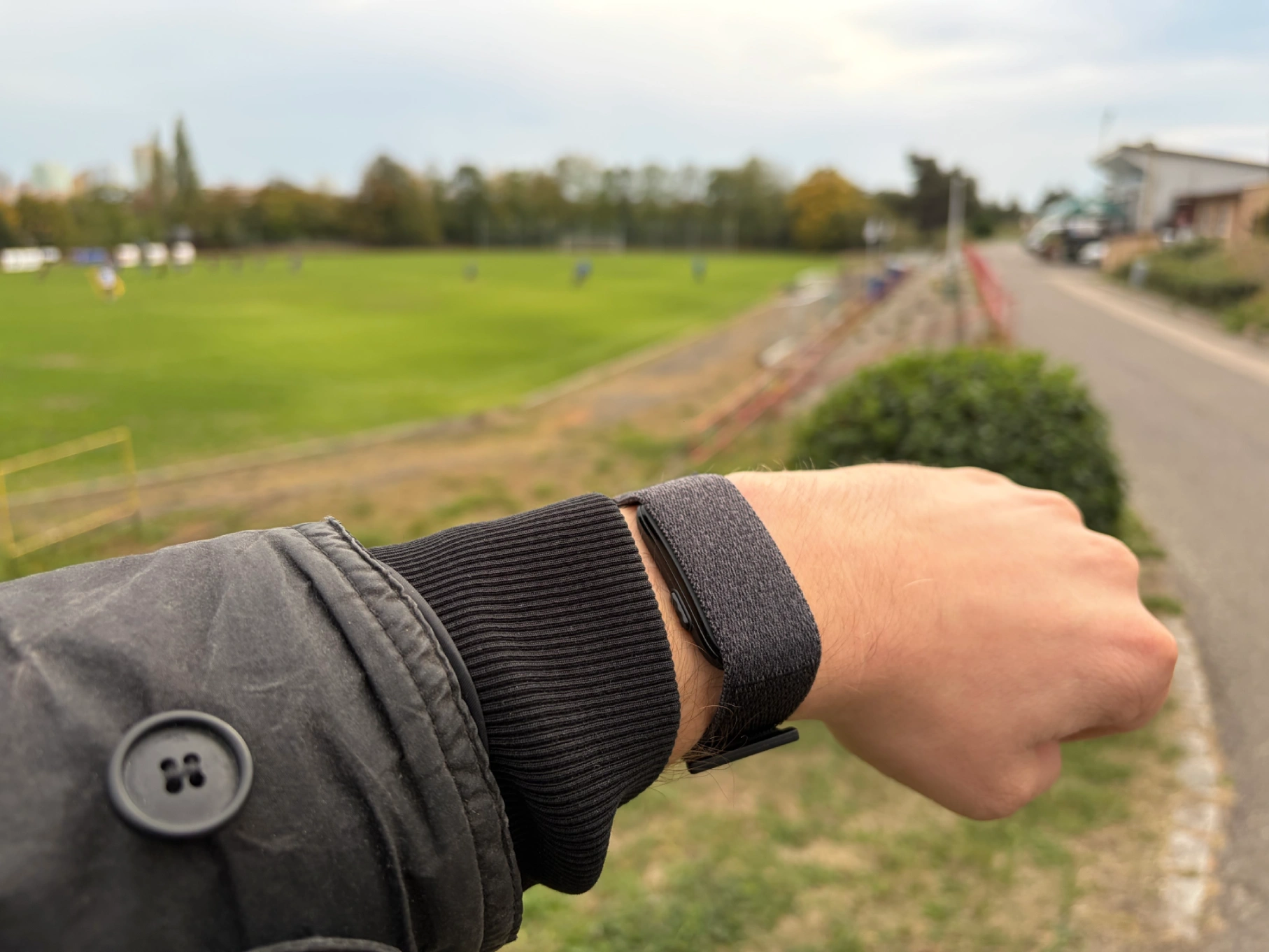 Ruka s chytrým náramkem Garmin CIRQA Smart Band Black před fotbalovým hřištěm